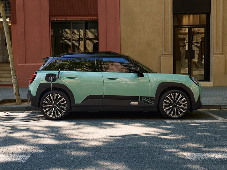 Side view of the all-electric MINI Aceman in Ocean Wave Green with Black Roof charging on the street.