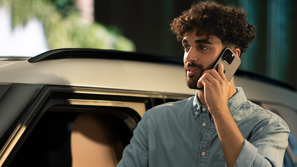 Person standing beside a MINI vehicle while talking on a smartphone.