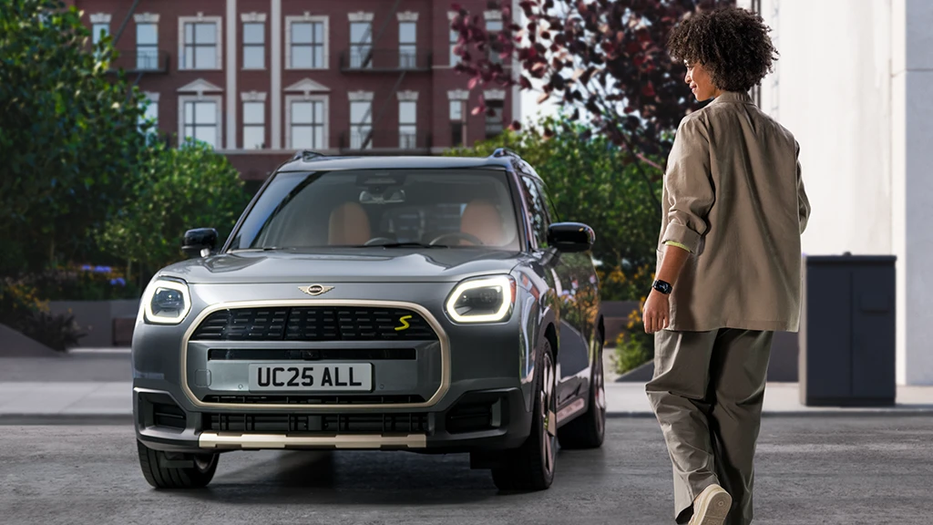 Person using a smartphone while standing in front of a MINI Countryman in Icy Sunshine Blue with a White roof.