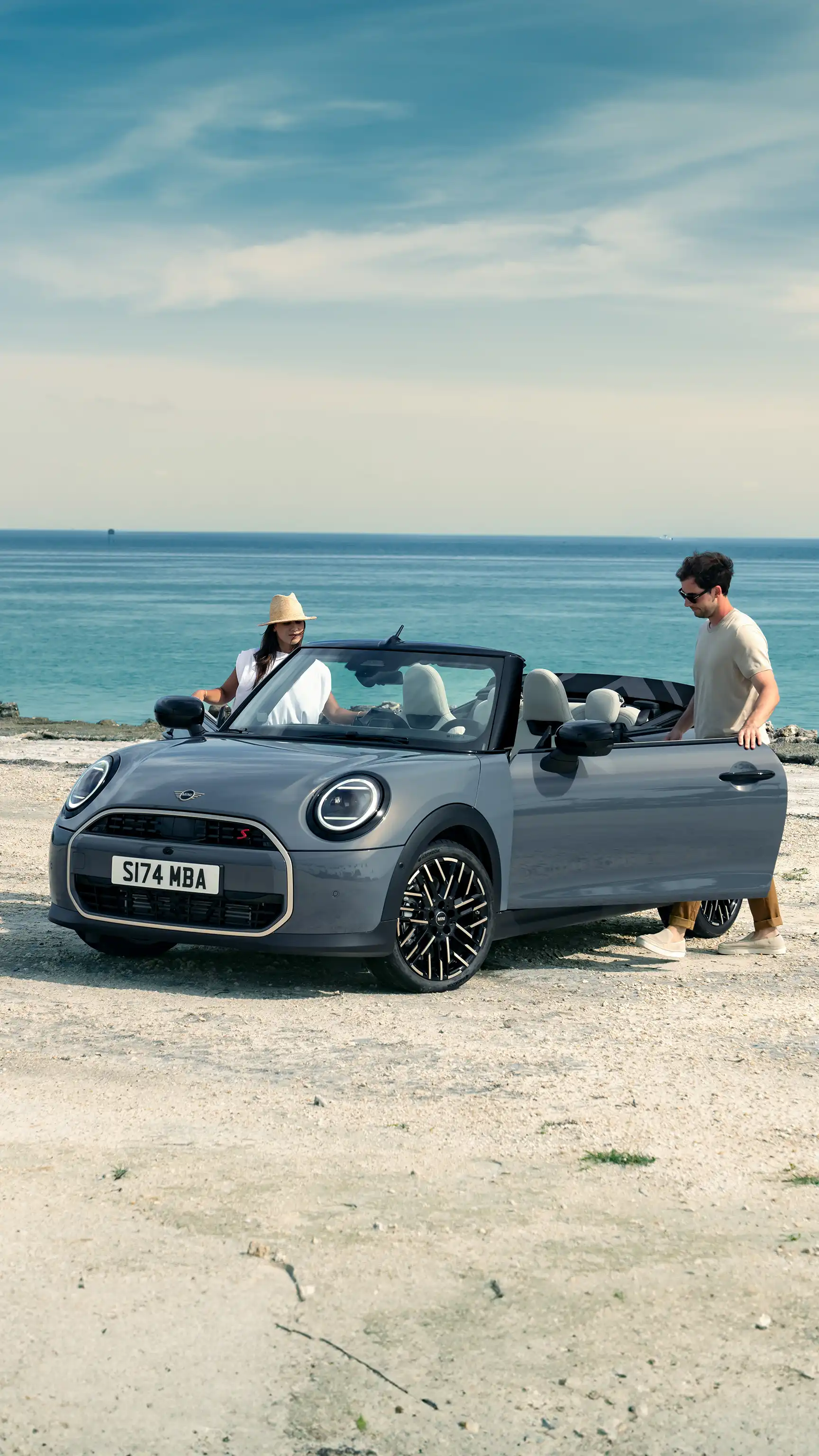 MINI Convertible in Melting Silver Metallic parked on a beachside while two people stand beside it.