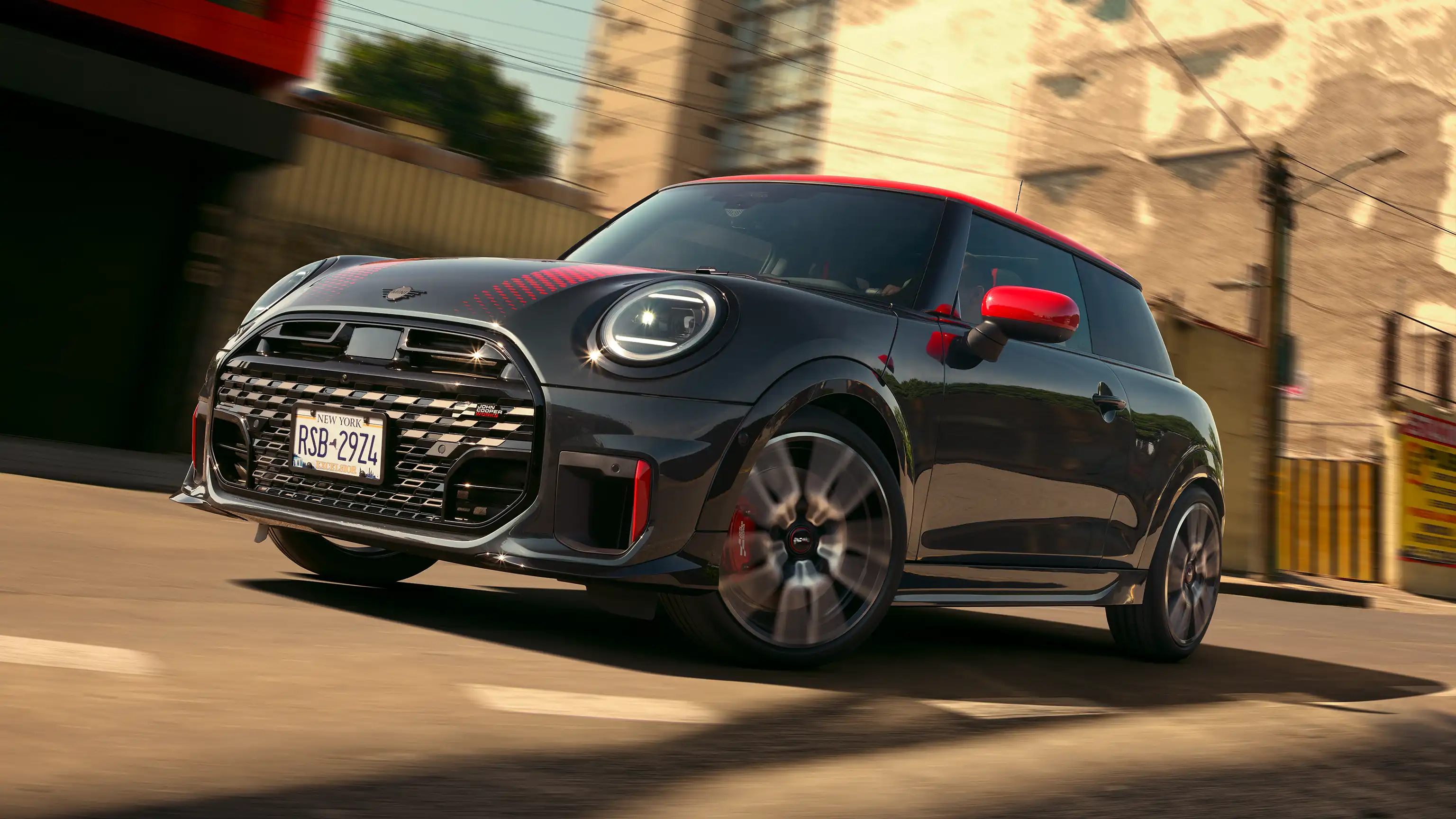 MINI John Cooper Works in Midnight Black II with Chili Red roof driving on an urban road.