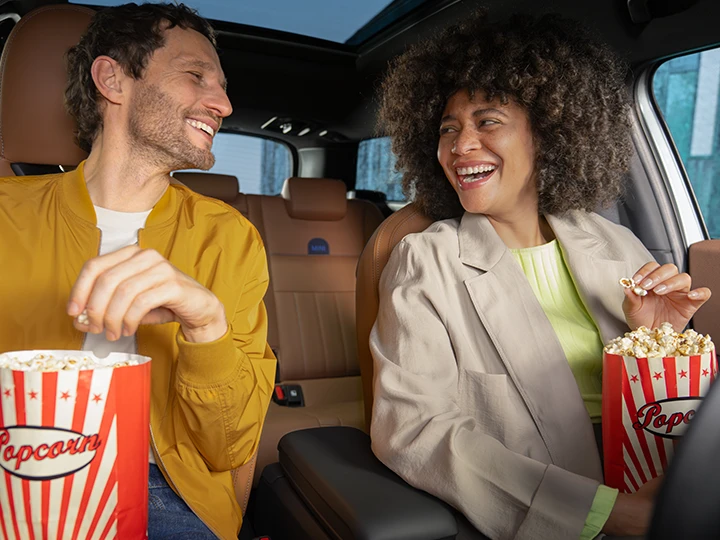 Two people sitting inside a vehicle enjoying popcorn.