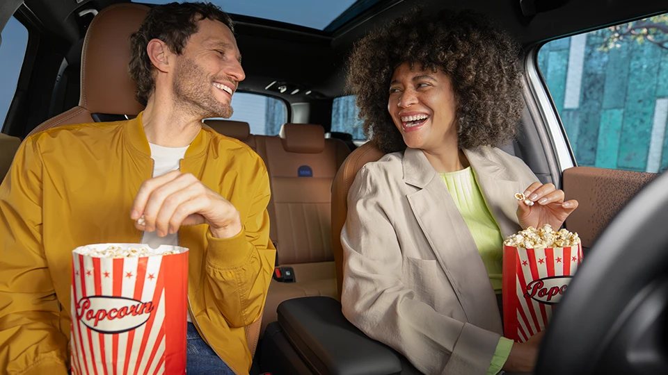 Two people sitting inside a vehicle enjoying popcorn.