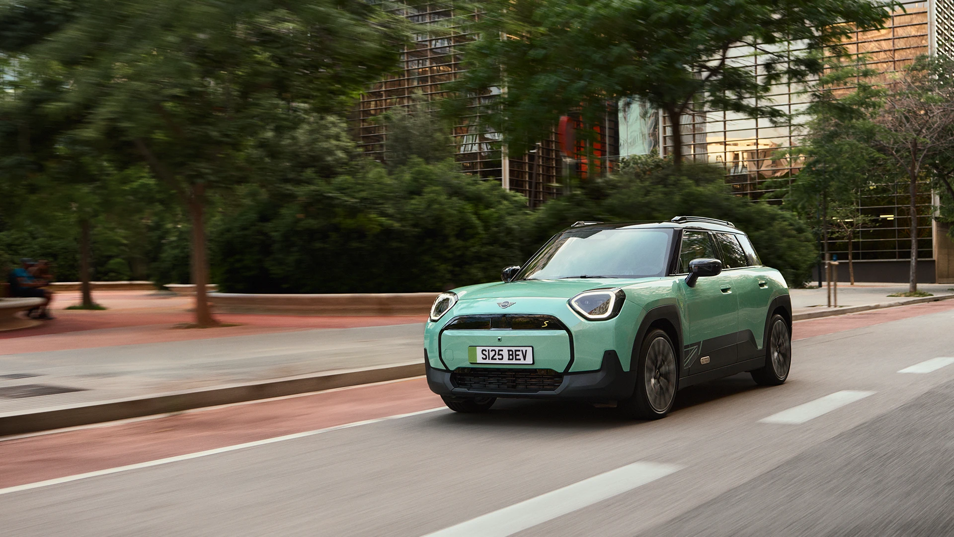All‑electric MINI Aceman in Rebel Green driving through a city street